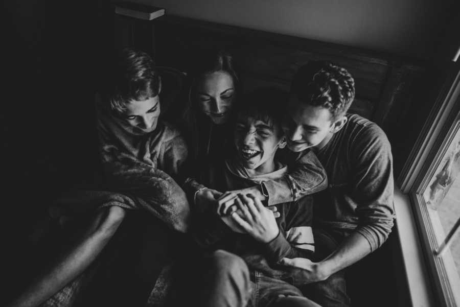 Three teens sit in bed hugging their adopted brother