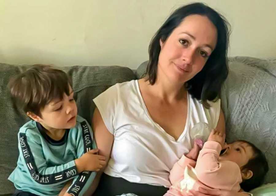 Single mother who struggles to do it all sits on couch with toddler and infant beside her