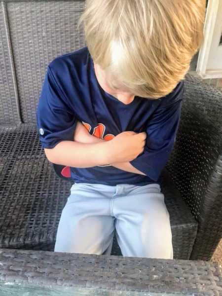 Young boy sits in chair with arms crossed looking down in a pout