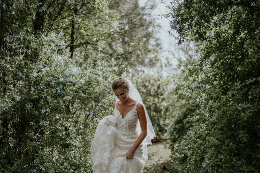 Bride walking through trail of trees in wedding gown