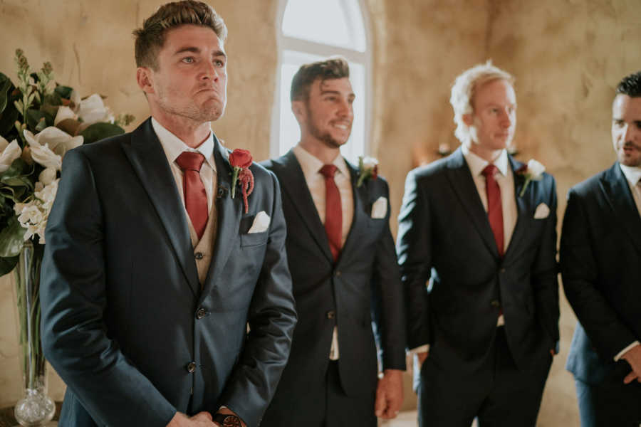 Groom holds back tears at altar next to groomsmen