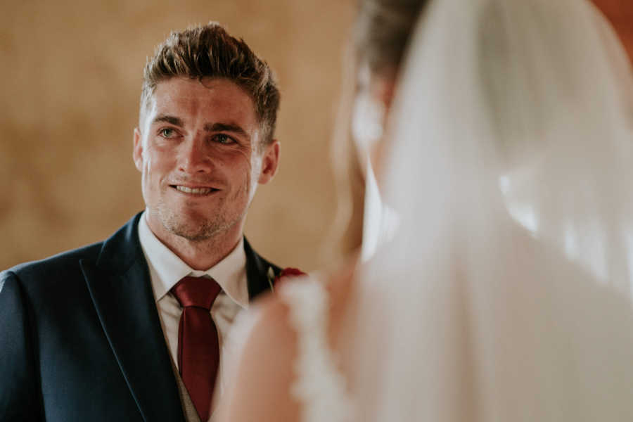 Groom whose father has cancer smiles off to side in front of bride
