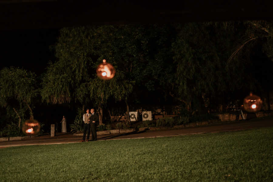 Groom and father who has cancer standing in distance outside at wedding reception