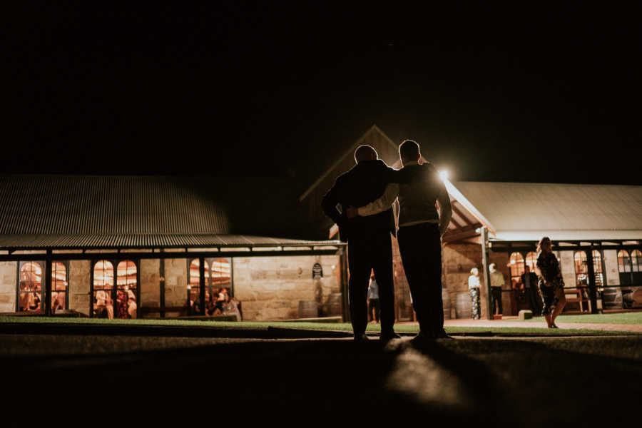 Groom whose father has cancer stands arm in arm with his father outside of wedding reception