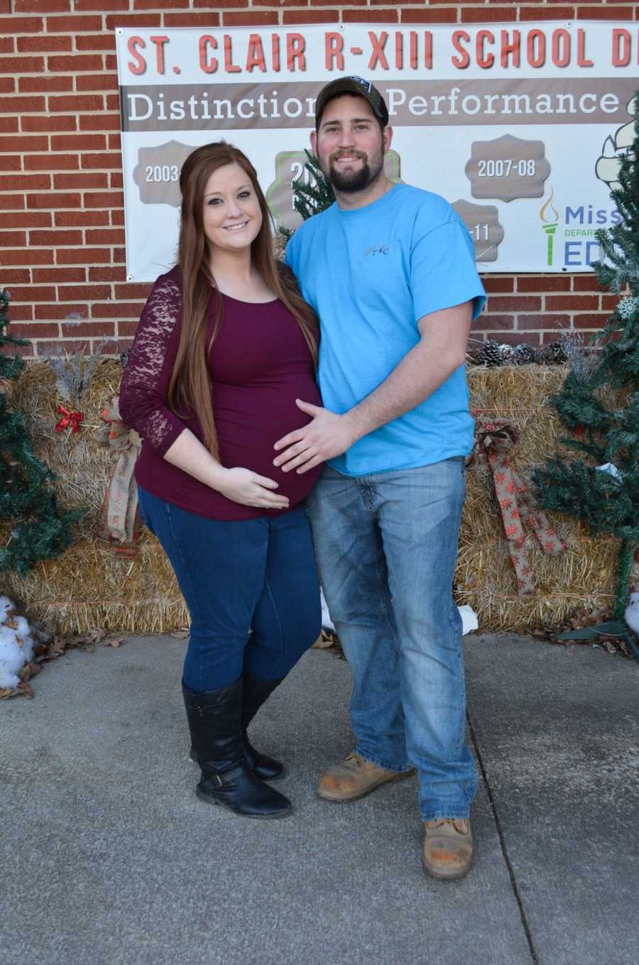 Pregnant woman and husband stand side by side smiling as they hold her stomach