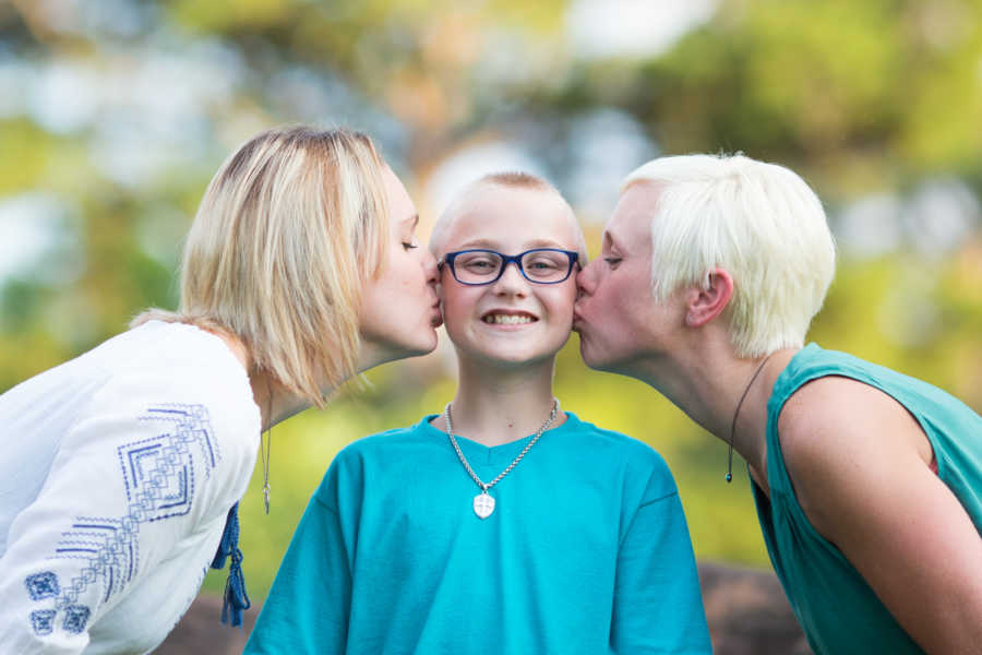 Biological mother and step mother kiss cheek of son