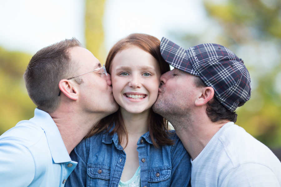 Biological father and stepfather kiss cheek of daughter