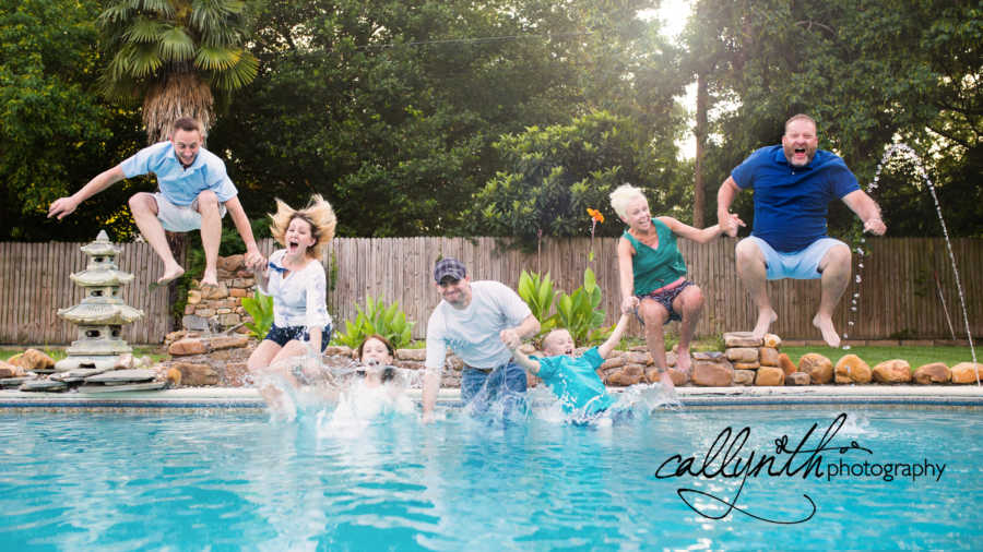 Family with three dads, two moms, and two kids hold hands while jumping in pool