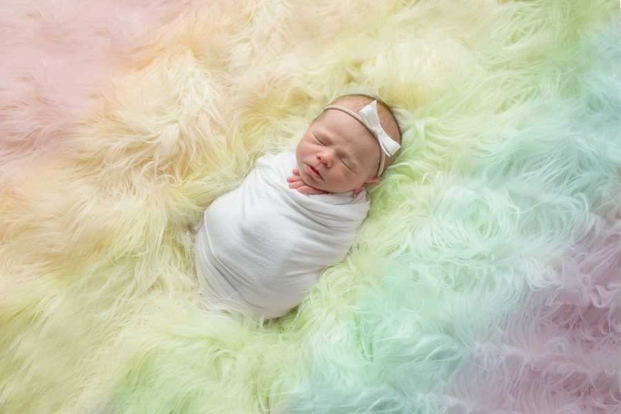 Newborn swaddled in blanket on rainbow carpet