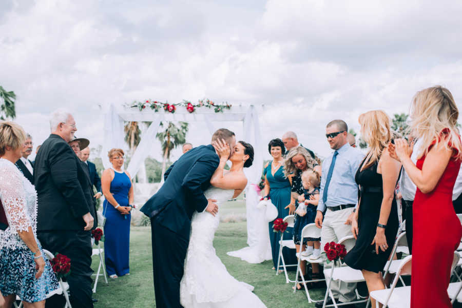 Bride and groom share kiss at outdoor wedding in front of guests