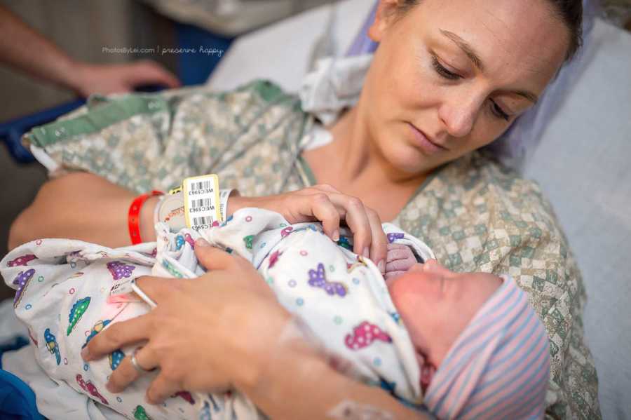 Mother looks down holding newborn in arms after c-section
