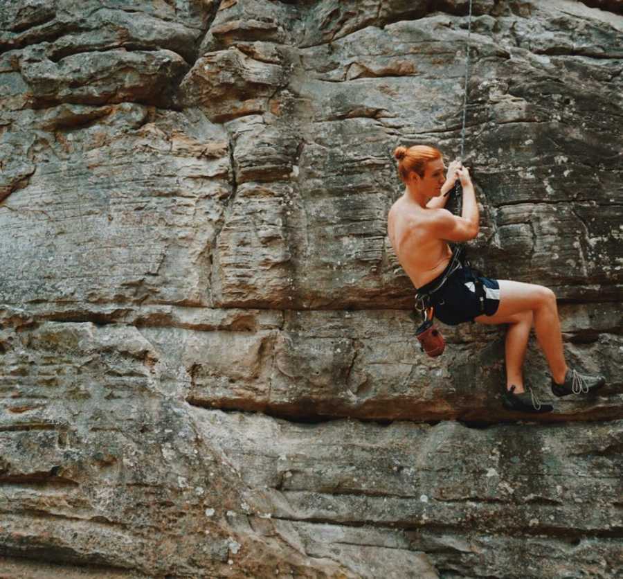 Man who has chosen fitness to combat depression hanging onto harness on side of cliff