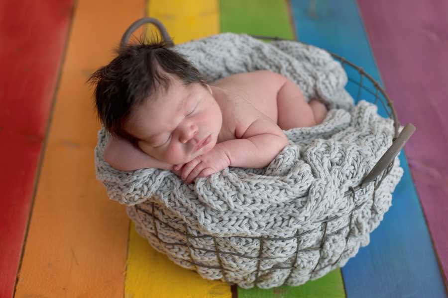 Newborn asleep in basket on rainbow floor