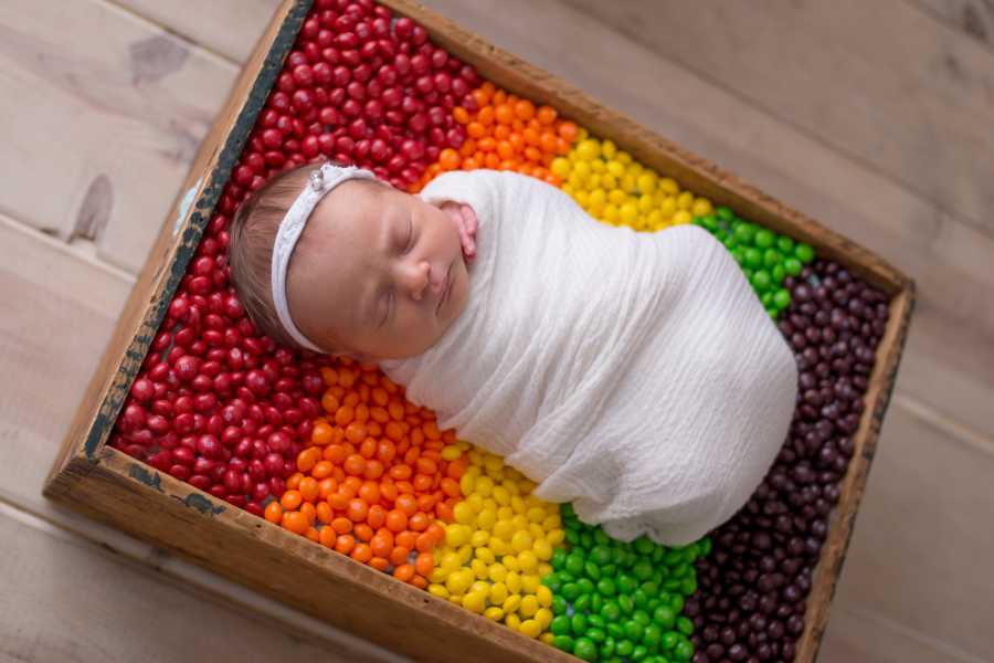 Newborn laying in wooden box on top of rainbow skittles
