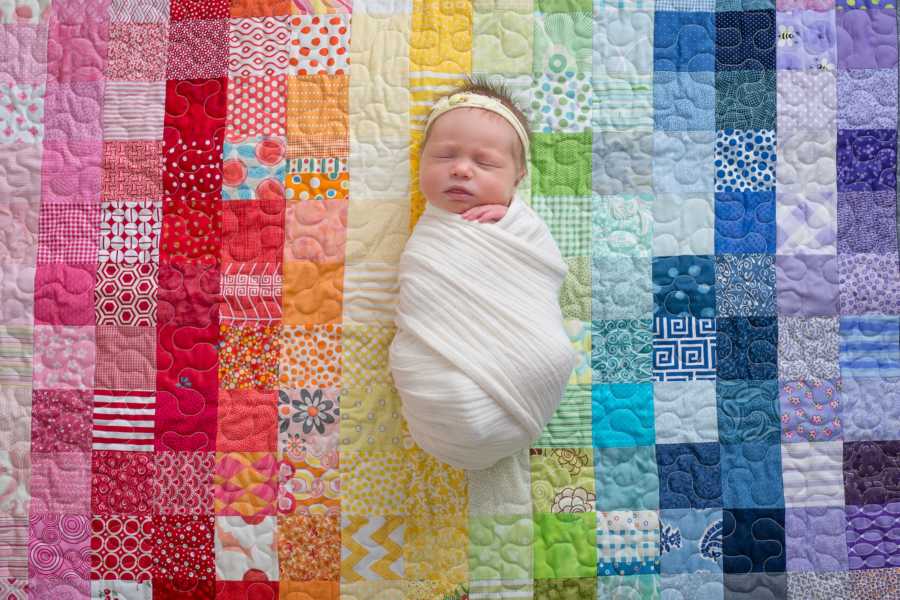 Newborn swaddled in blanket sleeping in rainbow quilted blanket