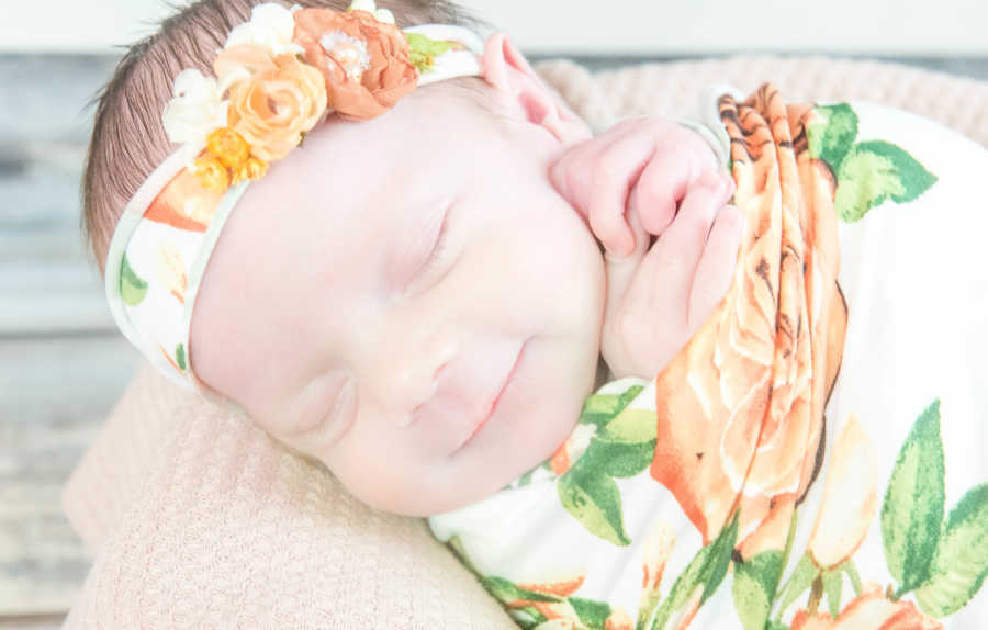 Baby with spina bifida and chiari malformation smiling while swaddled in floral blanket at home