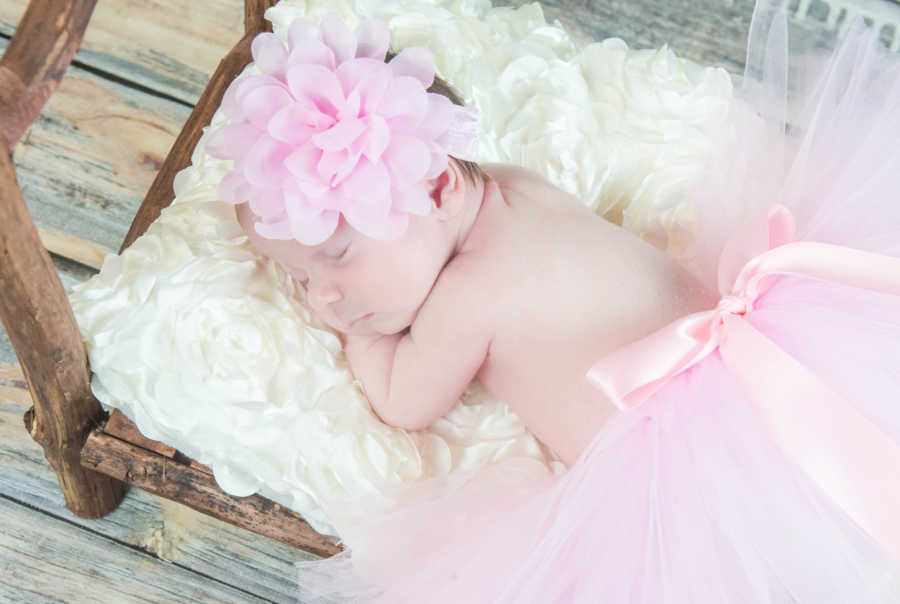 Baby with spina bifida and chiari malformation listen on floral bed with pink tutu and bow on her head