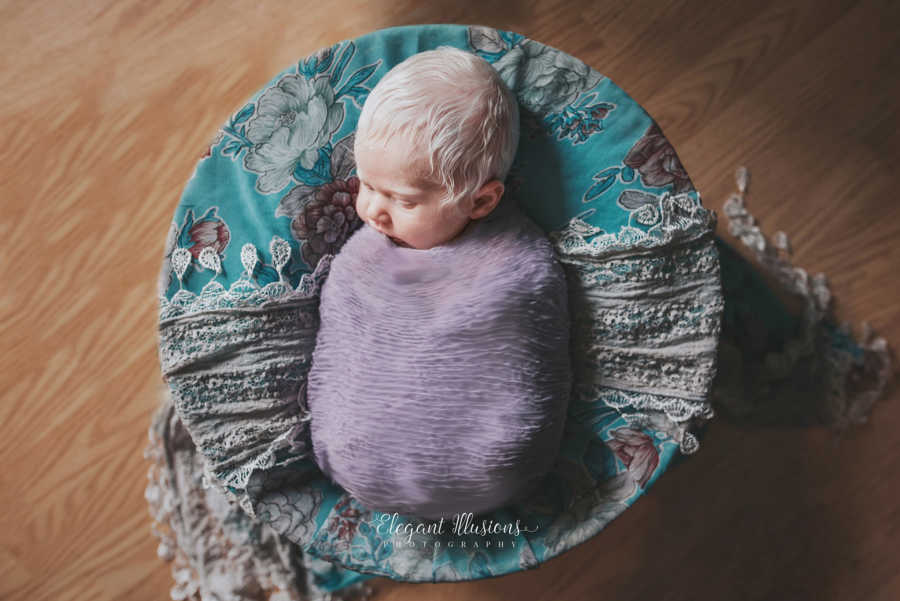 Aerial view of albino newborn with bright white hair swaddled in purple blanket