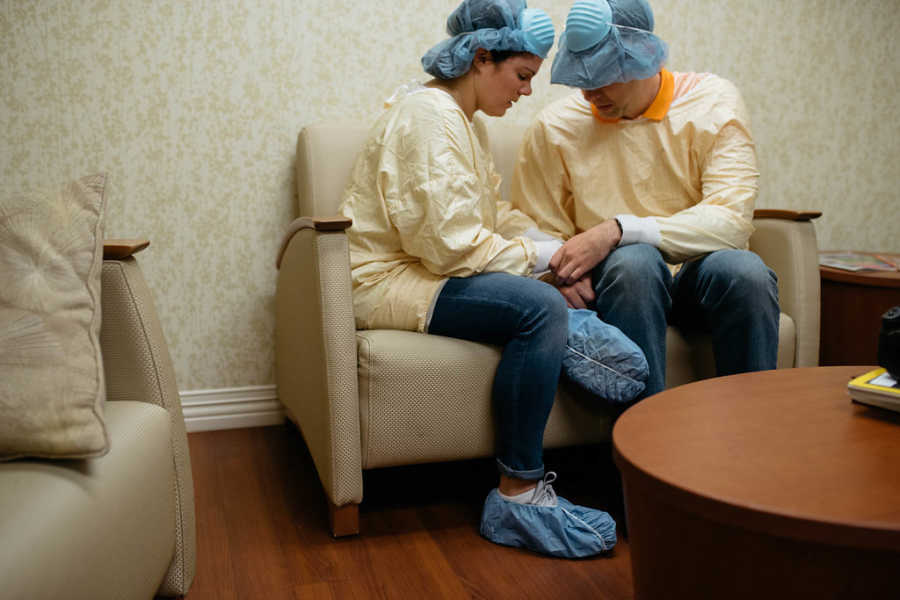 Husband and wife sit in waiting room holding hands awaiting the birth of their adopted child