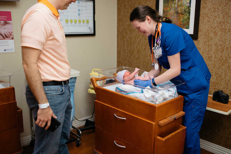 Nurse picks up newborn baby while adoptive father stands next to her