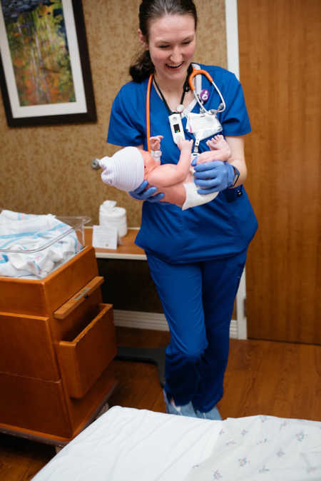 Nurse smiles while holding newborn baby
