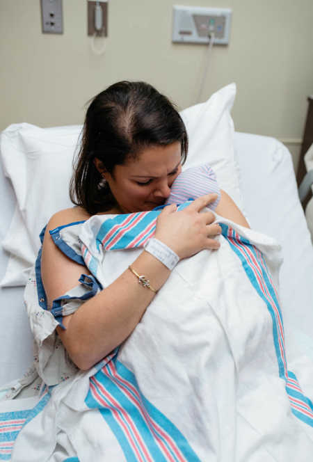 Mother holds newborn adopted baby skin to skin in hospital bed