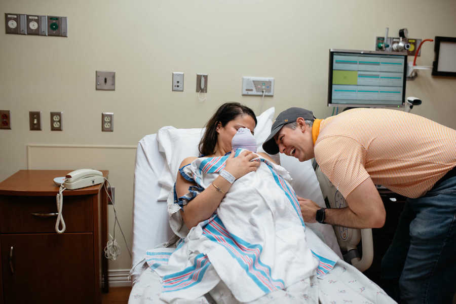 Woman holds adopted newborn towards her husband for him to see baby's face