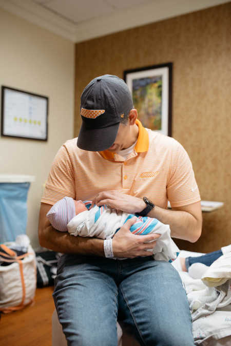 Father holds adopted newborn in his arms in hospital room