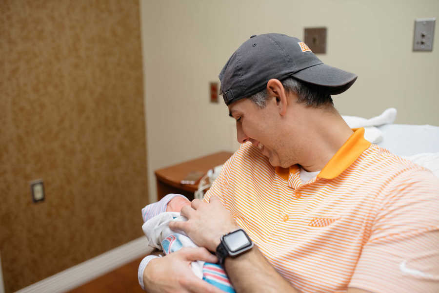 Father smiles down at adopted new born he holds in his arms