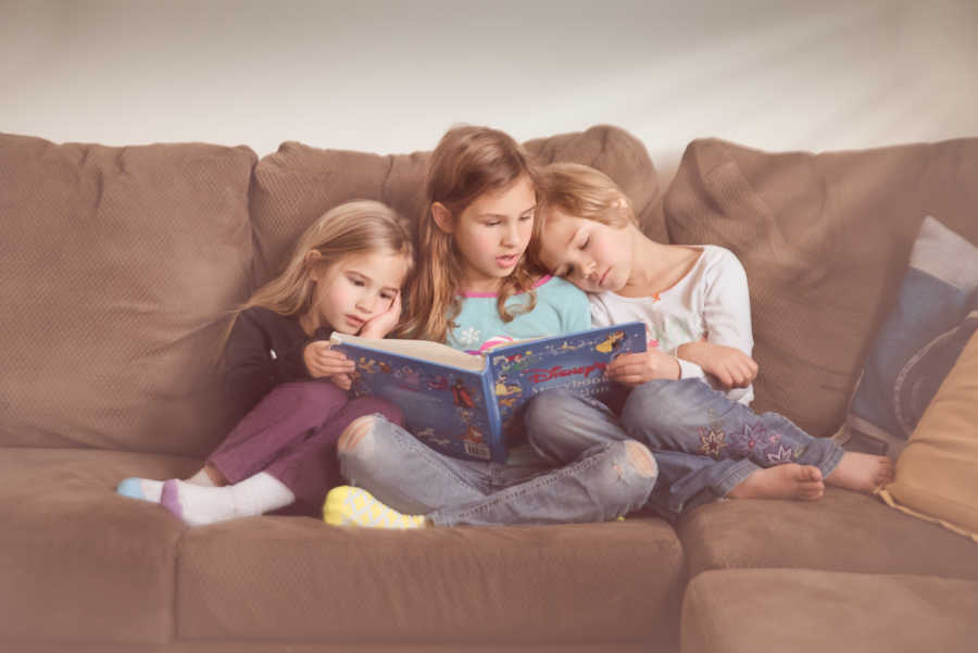 Three daughters of woman who suffered from a miscarriage sit on couch reading book together