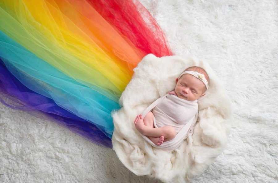 Newborn lays on fluffy white material attached to rainbow fabric