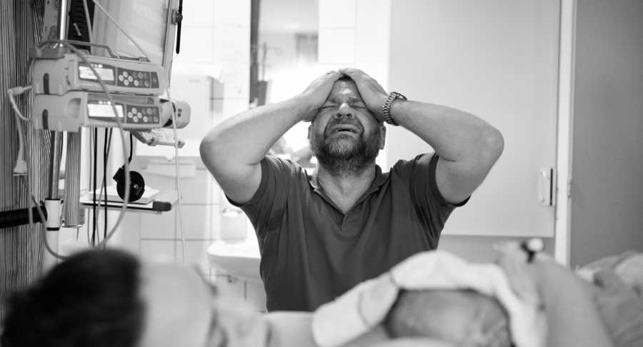 Husband holds hands to his forehead looking up to sky after wife gave birth