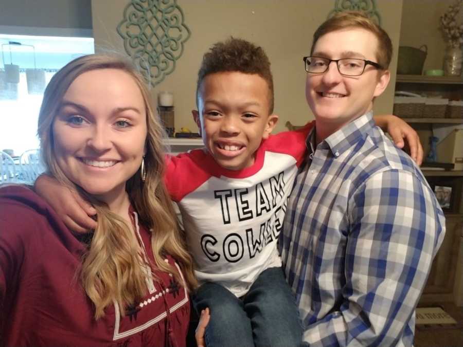 Mother and father smile in selfie while holding adopted son