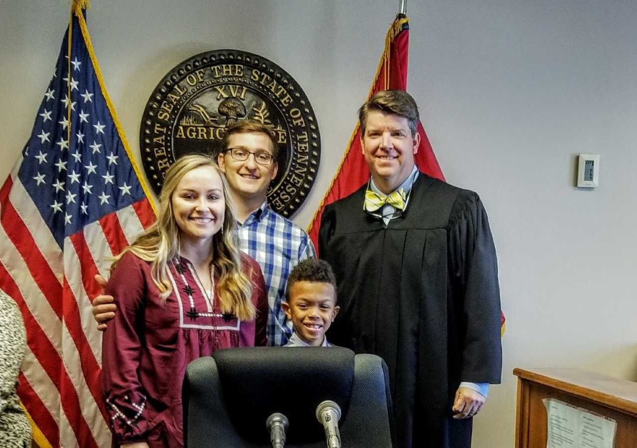 Mother and Father stand next to judge and adopted son at adoption court