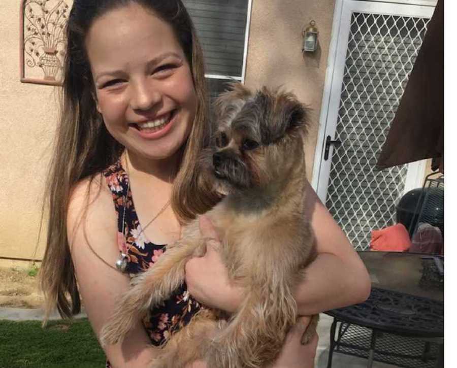 Young girl who defied doctor's diagnosis of not living long smiling while holding little dog