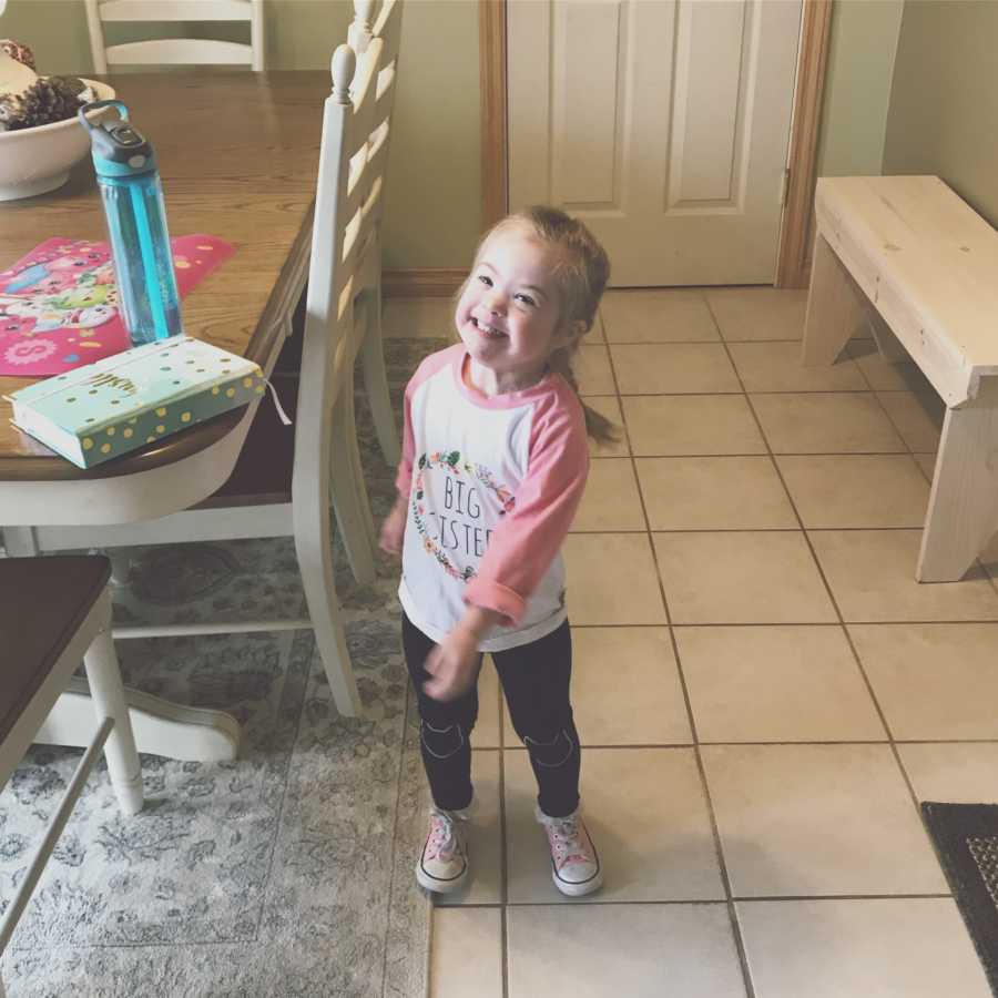 Little girl with down syndrome smiling next to table in home