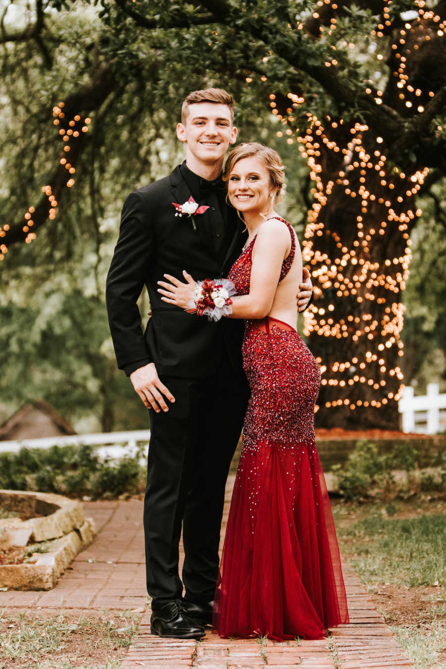 Boyfriend and girlfriend smile with arms wrapped around each other after getting engaged on prom night