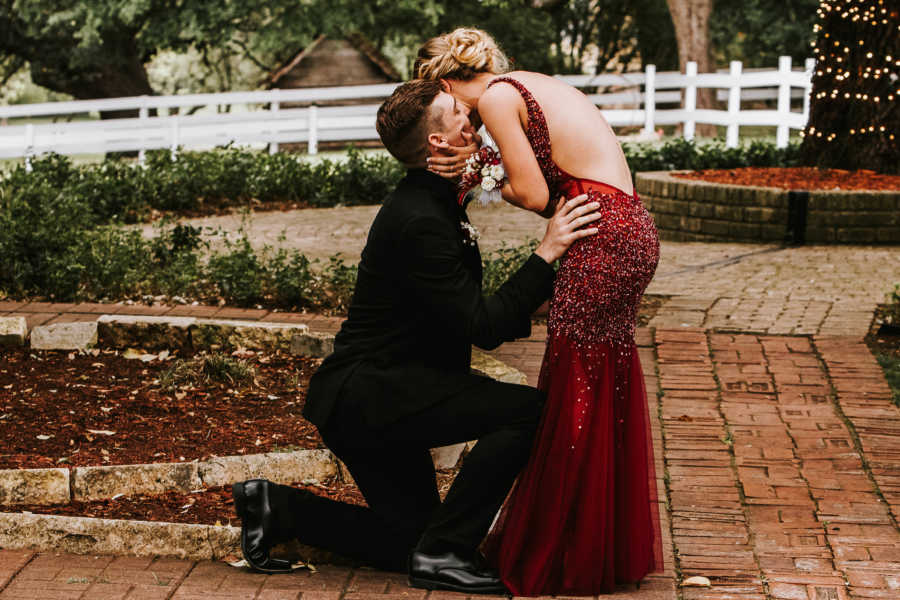 Girlfriend in prom dress leans down to kiss boyfriend who just proposed