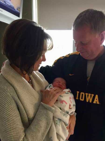 Husband and wife who adopted their daughter admiring their newborn grandchild