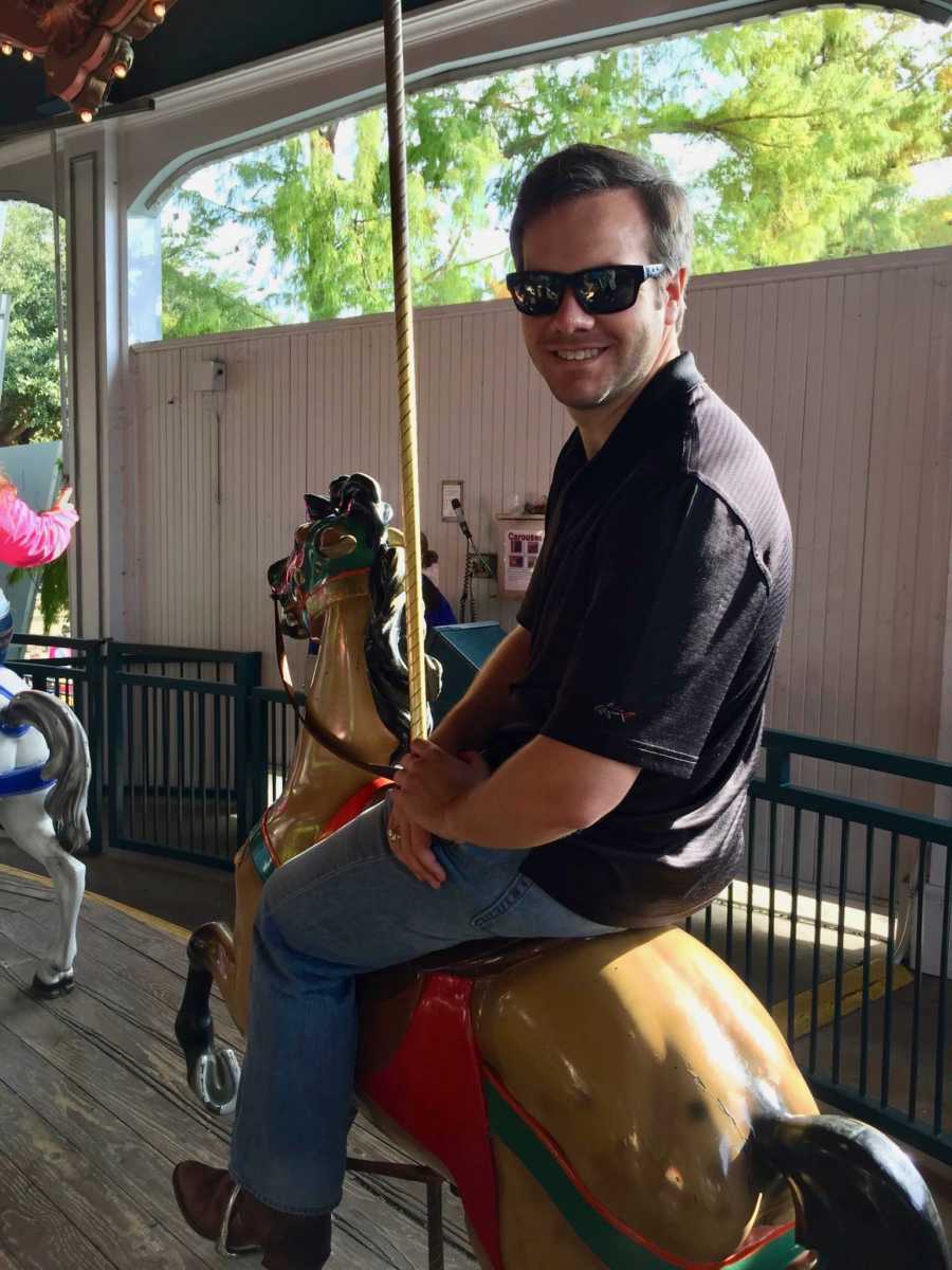 Husband of wife who says she doesn't need him sitting on a horse of merry go round