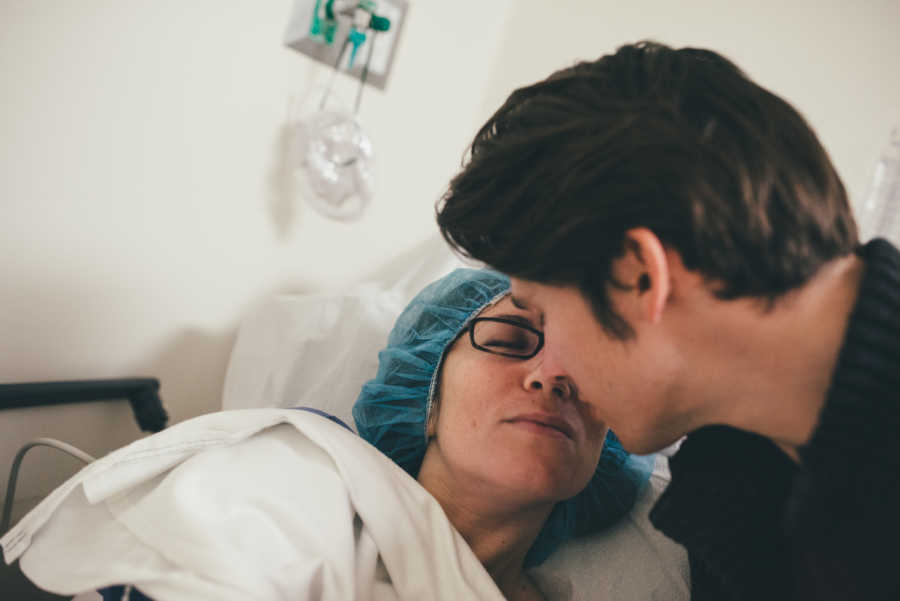 Photographer who struggled with infertility lies in hospital bed as husband leans over to kiss her