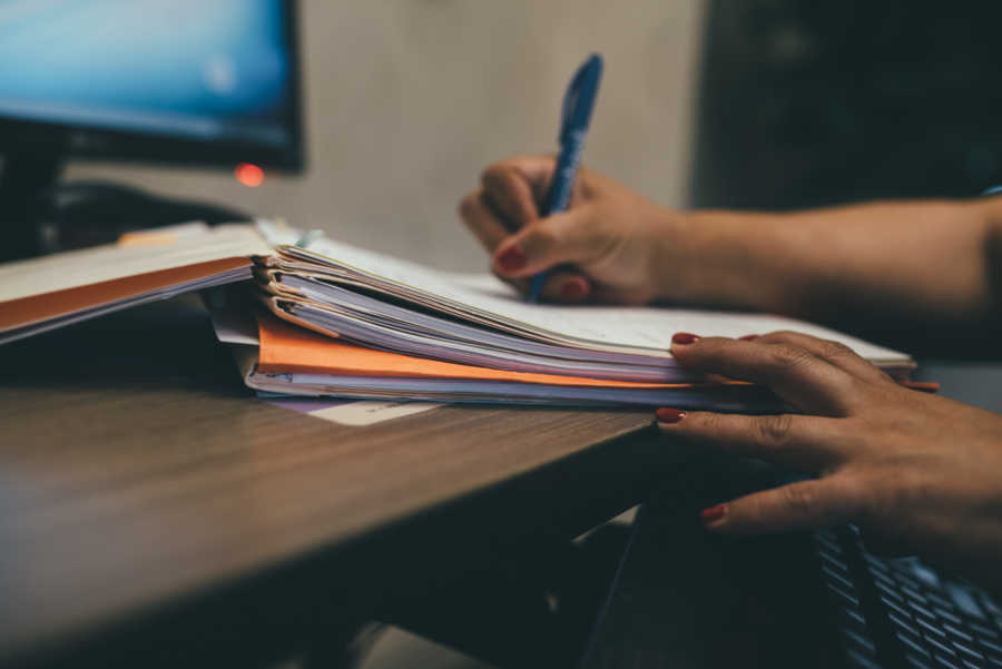 Woman writing on paper on stack of paperwork