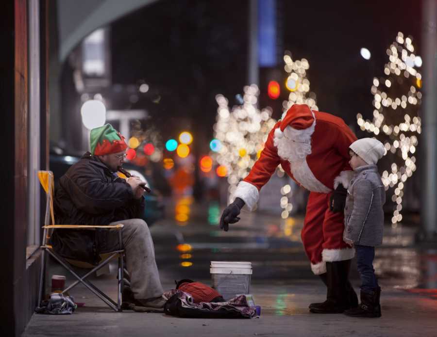 Child of man who passed away stands with man in Santa suit in front of man playing flute for money