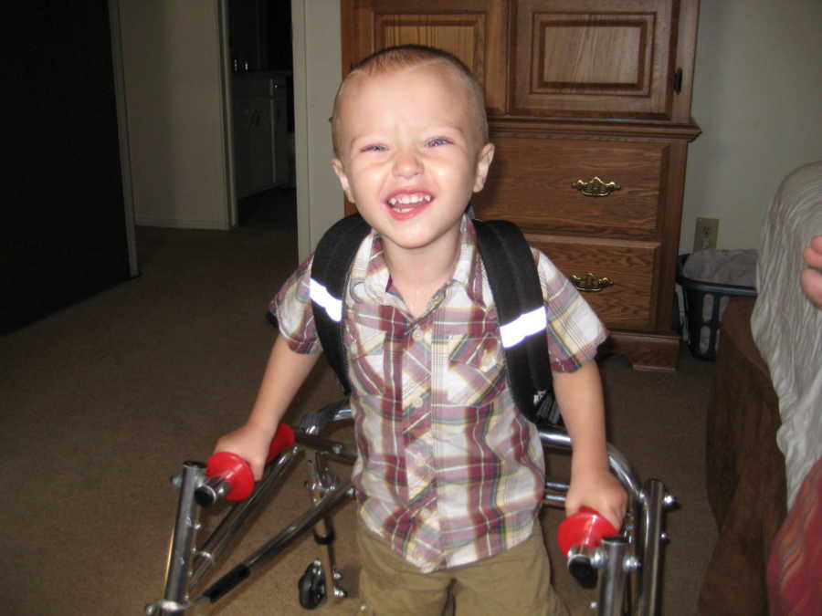 Toddler with cerebellar atrophy holding on to walker smiling