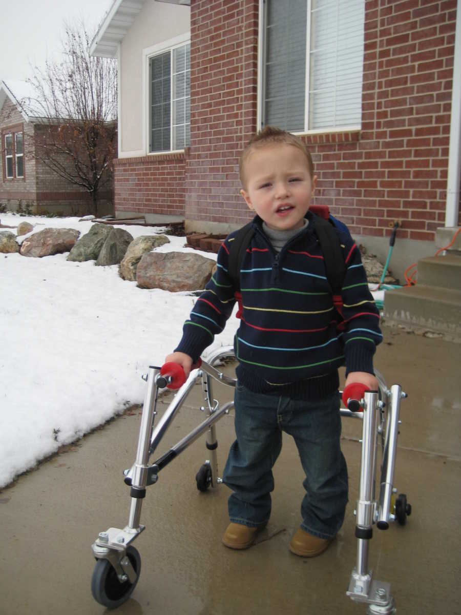 Toddler with cerebellar atrophy walking with walker outside of house