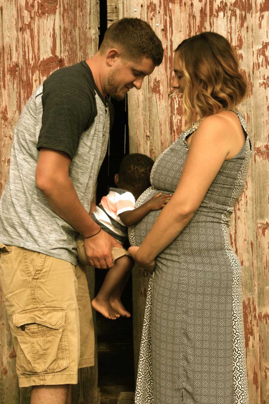 Father holds adopted son to pregnant wife's stomach while he wraps his arms around her
