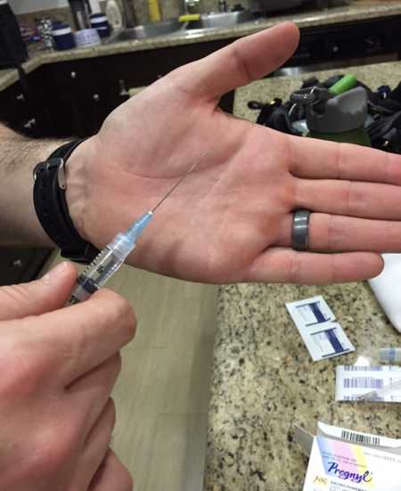 Husband of wife who struggles to get pregnant holds out hand with IVF needle in front of it