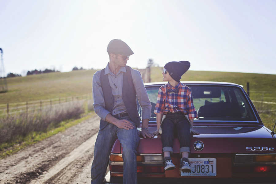 Father sits on trunk of old red BMW beside son