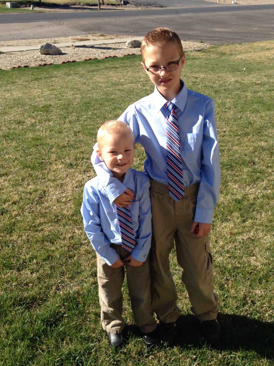 Young boy with cerebellar atrophy standing with arm around younger brother in matching shirt and tie