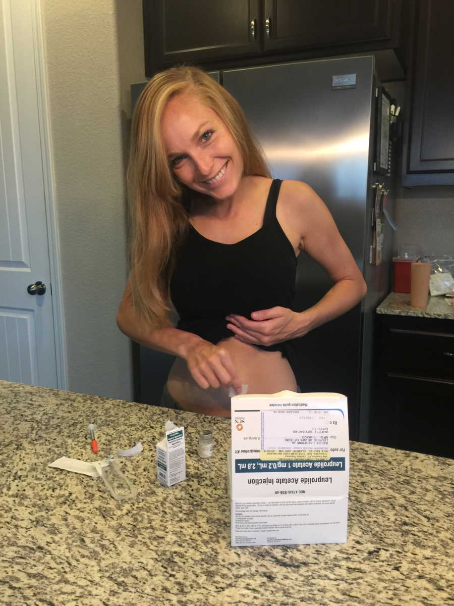 Woman smiling in kitchen with her shirt up prepping her stomach for IVF treatment